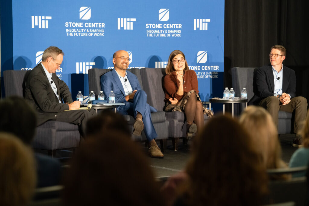 Four panelists sit in armchairs onstage