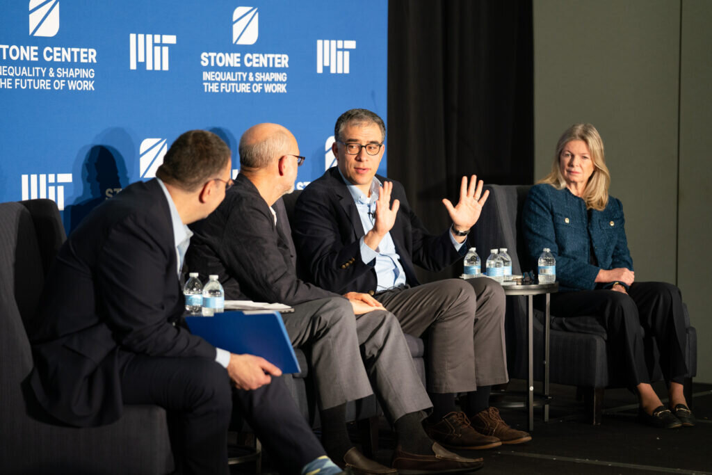 Four panelists sit in armchairs onstage