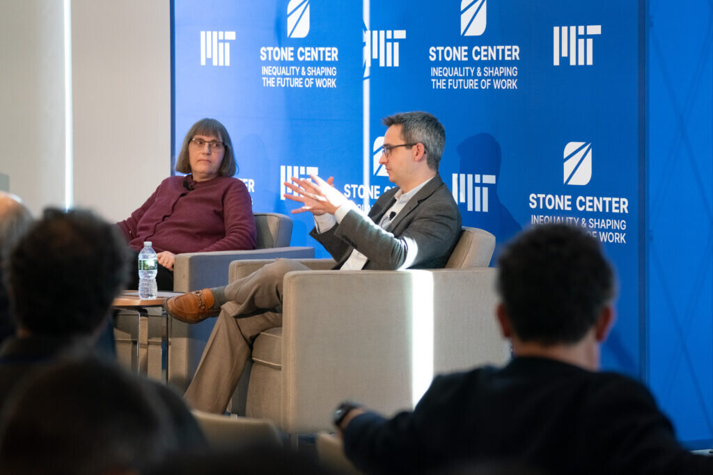 Two panelists sit in armchairs on stage in front of a blue Stone Center banner.